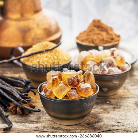 Crystals caramel brown sugar, natural vanilla pods, star anise, sugar cane, cocoa powder in old metal cup on a wooden background. selective Focus