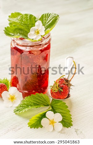 Strawberry jam in a glass decorated with leaves and flowers of strawberry. selective Focus