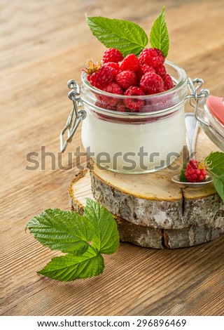 Glass jar with homemade yogurt and fresh garden raspberries on a wooden background. The concept of healthy homemade food. selective Focus
