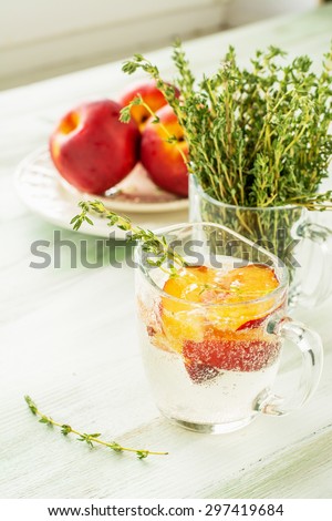 Sweet fizzy drink with peach slices and thyme on a light background. selective Focus