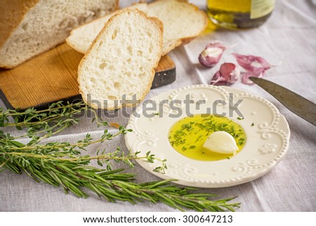 Fresh homemade white bread and a plate with olive oil, garlic and herbs on a light textile background. selective Focus