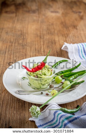 Green hot sauce with young garlic in portion bowl on wooden background. selective Focus