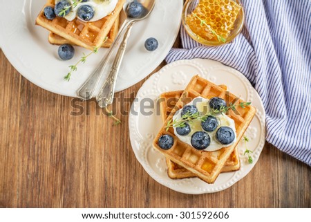 Homemade fresh crispy waffles for breakfast with fresh blueberries and honey on a ceramic bowl and a wooden background. selective Focus