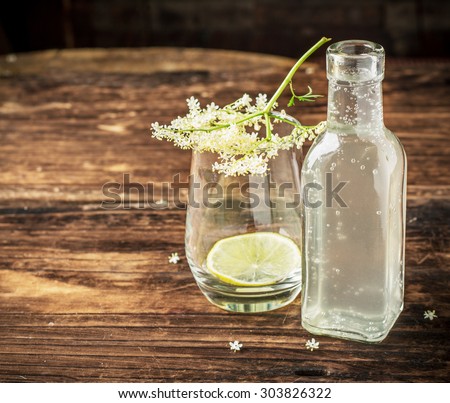 Bottle with a drink from the elder and an empty glass with a sprig of elder on a dark wooden background. selective Focus