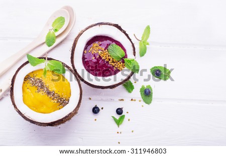 A healthy breakfast smoothie mango and berries garnished with chia seeds and bee pollen in two coconuts on a light wooden background. Concept of healthy food. Top view. selective Focus