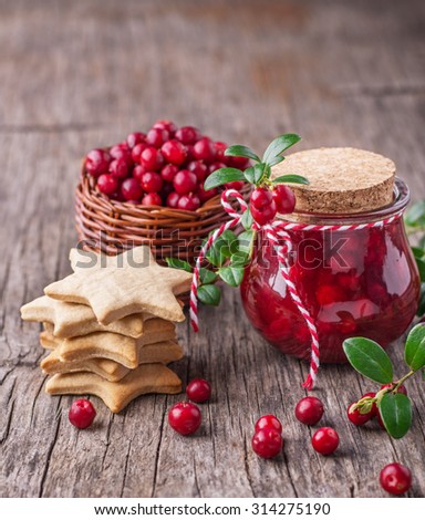 A small jar of homemade fresh spicy sweet cranberry sauce with cinnamon next to a stack of homemade gingerbread cookies in the shape of stars on a dark wooden background. selective Focus