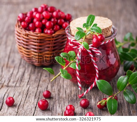 A small glass jar with fresh homemade cranberry sauce on a wooden background with ripe cranberries. selective Focus