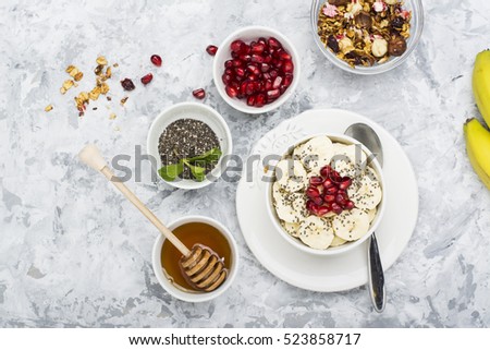 Healthy breakfast oatmeal with pomegranate, bananas, seeds and nuts, overhead scene on white marble