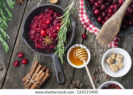 Fresh homemade cranberry sauce in a pan on dark wooden background with scattering of ripe berries. Top veiw
