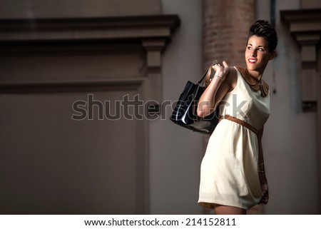 happy italian young modern caucasian lady with short hair with elegant dress and with purse in hands walking on the streets