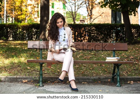 Young woman caucasian asian smiling and sitting on a bench reading a book in the park