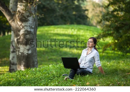 Mature woman happy on laptop sitting on the grass in the park