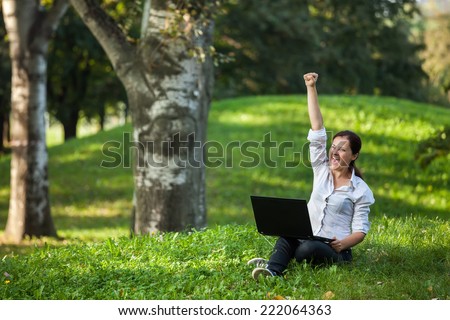 Excited mature woman wining holding fist up high screaming of happiness with laptop