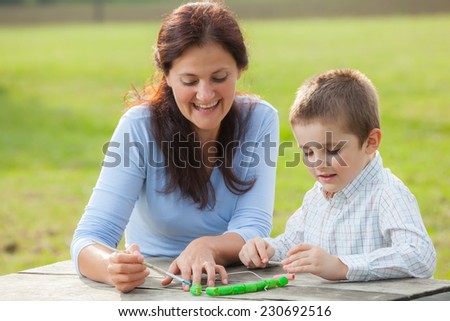 Young woman teacher teaches little young boy in white shirt painting with the brush to make  pasta beads