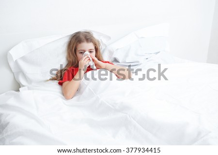 cold sick child laying on bed and blowing her nose in tissue