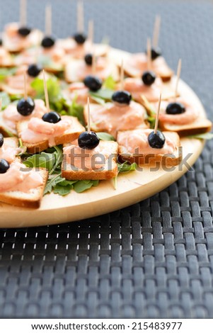 Closeup of snacks with salmon sauce,shrimp and black olives on ruccola leaves.