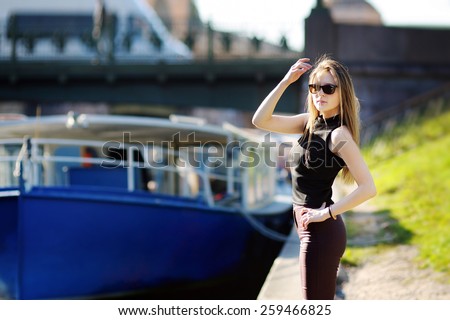 Lovely young woman, blond, slender, with long straight hair, glasses, t-shirt posing against the backdrop of boats