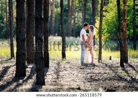 young family man and a pregnant woman, a blonde with curly hair dilnnymi, bright long dress, go in the woods, in the light of the sun