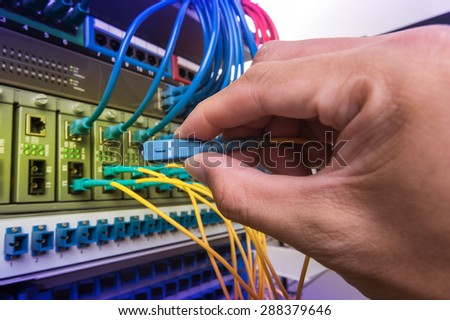 Man connecting fiber network cables to switches