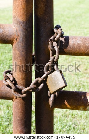 Color photograph of a old rusty lock and chain holding together a metal gate.