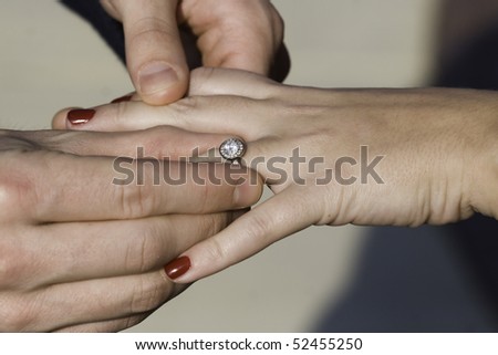 Color photo of a man putting an engagement ring on a female\'s hand.