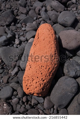 One single orange stone is surrounded by black stones - taken on a beach of Lanzarote, Canary Islands, Spain.