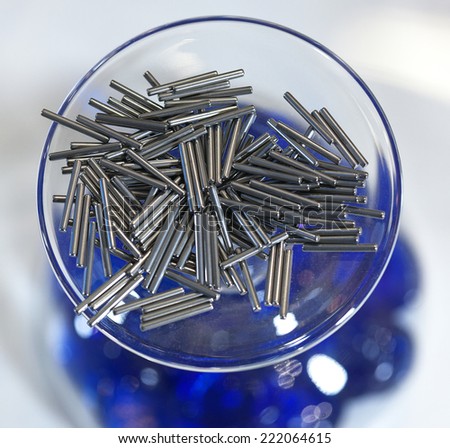 Small silver metal pins in a glass bowl in front of a blue and white background