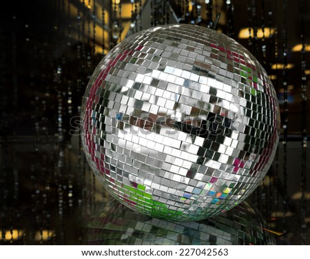 A silver mirror ball lies on a reflective glass surface in a darkened room.