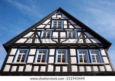Upper part of an old, restored half-timbered house - black and white facade with white windows and blue window frames