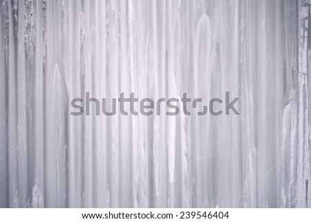 Blurred structure of a run down paint on a glass surface in white and gray with fine dark spots