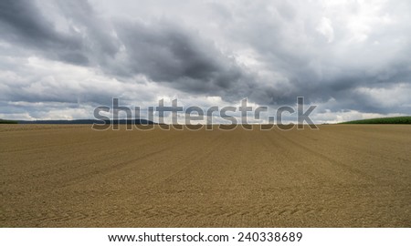 Newly harrowed field of brown earth with dark thunderclouds, taken on an autumnal day in Germany.