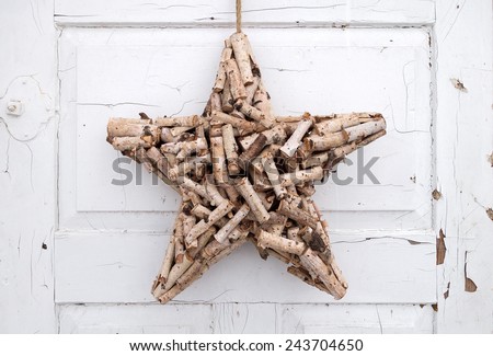A handcrafted star made of natural, short cut branches hangs on an old, white-painted door. The color is dirty, cracked and partially already peeled off.