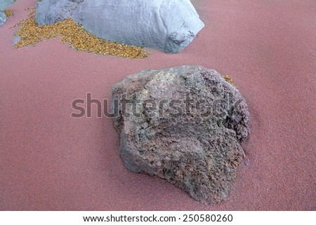 Detail shot of two gray rocks in the reddish sand. As well there lay brown, withered plant parts they were blown by the wind.