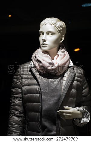 Upper body of a female mannequin with a gray quilted anorak and a round the neck scarf in front of a dark background