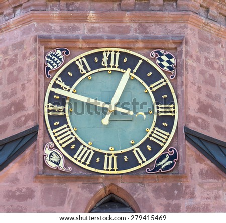 Detail of a round, black and golden church clock with roman numerals in a red facade. Taken at the town church in Freudenstadt, Germany.
