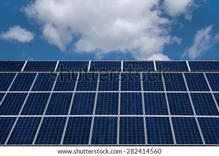 Blue solar cells with white border against blue and white sky. All-over mounted on a rearwardly inclined roof area.