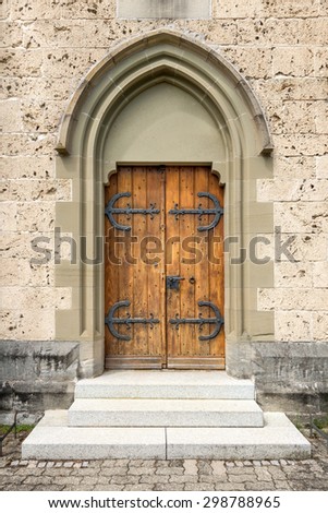 Brown wooden church door with large ornate metal fittings in a gothic stepped portal