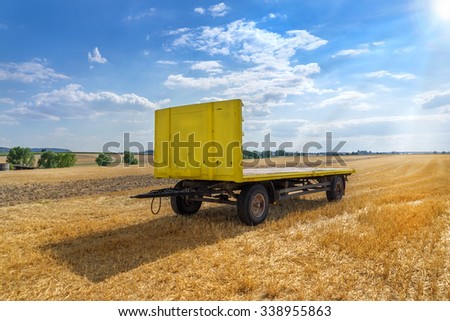 Big yellow trailer with open loading area in a stubble field in rural landscape
