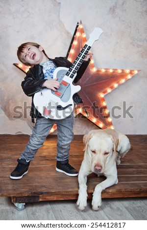 little cute boy playing guitar and singing like a rock-star for his dog labrador retriever