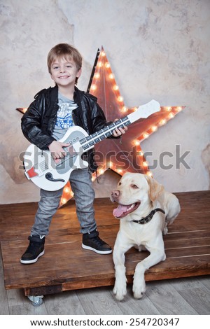 little cute 4 years old boy playing guitar and singing like a rock-star for his dog labrador retriever
