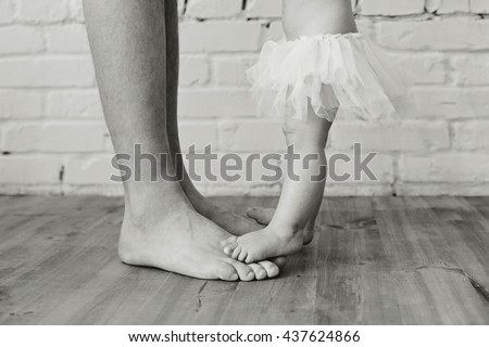 Child with Father Together. Feet Barefoot on wooden floor. Healthy Lifestyle. Close up of dad and little daughter feet at home. Bare baby and dad feet with tutu. Concept of friendly happy family.