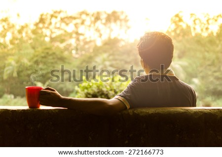 Young man relaxing in a garden having hot coffee in afternoon