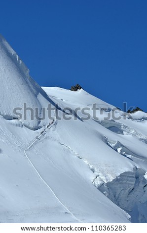 Team of unidentified climbers climbing a steep ice slope, roped together above a giant  crevasse, in perfect conditions under a blue sky