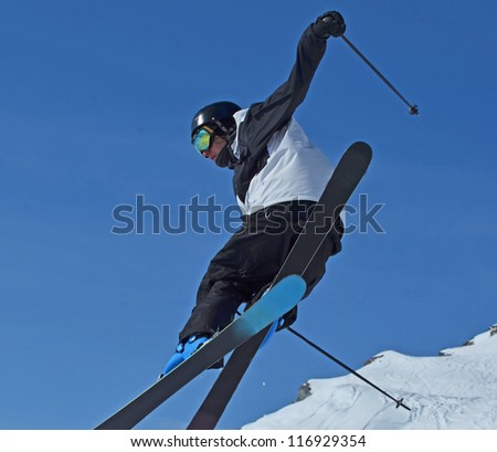 a ski jumper in black and white performs a high jump against a blue sky
