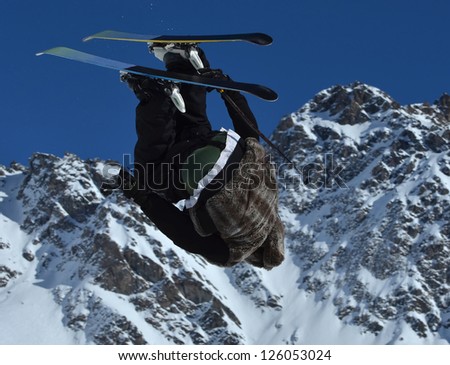 A stunt skier performing a 360 degree loop and ski grab at the same time, against a clear blue sky.