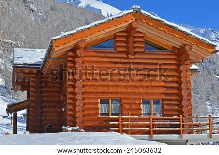 An alpine log cabin with snow covered mountains and forests in the background