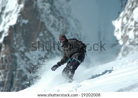 Snowboarder on the Mt Blanc, in deep powder snow, with the backdrop of the Mt Blanc de Tacul a 4000m summit in France. The flash of powder snow gives the shot movement, and some excitement