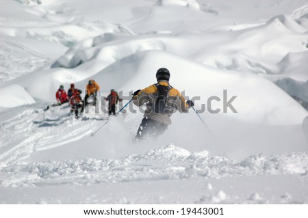 A skier being watched by his friends as he skis down through powder snow on the Giant's Cascade on the Mt Blanc, France.  In the background powder snow covers the crevasses