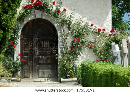Doorway framed with roses to a mortuary in a swiss mountain cemetery.  To either side gravestones.