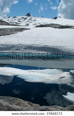 Snow floating in lake at the foot of the Diablerets glacier, with reflections of snow banks and fair weather cumulus clouds in the clear waters. On the glacier, two ski lifts can be made.